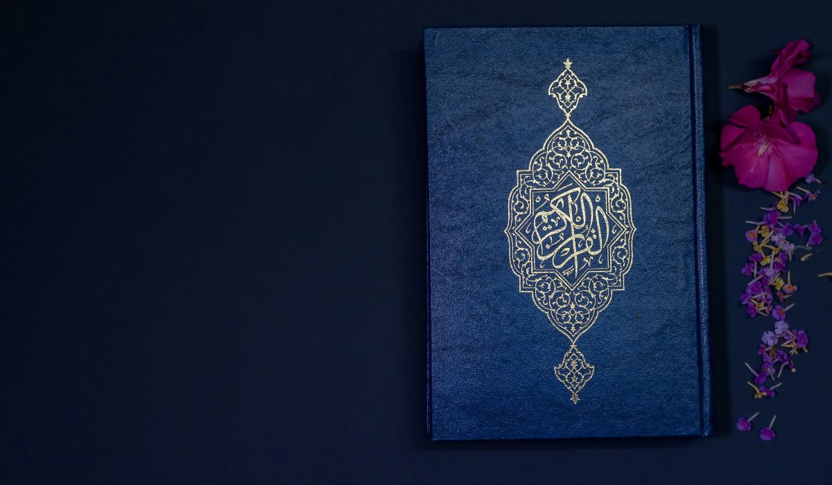 Coran bleu orné de motifs dorés, posé sur un fond sombre avec des fleurs roses