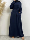 Une femme porte une abaya bleu marine, simple et élégante, avec une ceinture assortie nouée à la taille