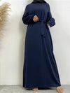 Une femme porte une abaya bleu marine avec une ceinture assortie nouée à la taille. Elle complète sa tenue avec un hijab noir