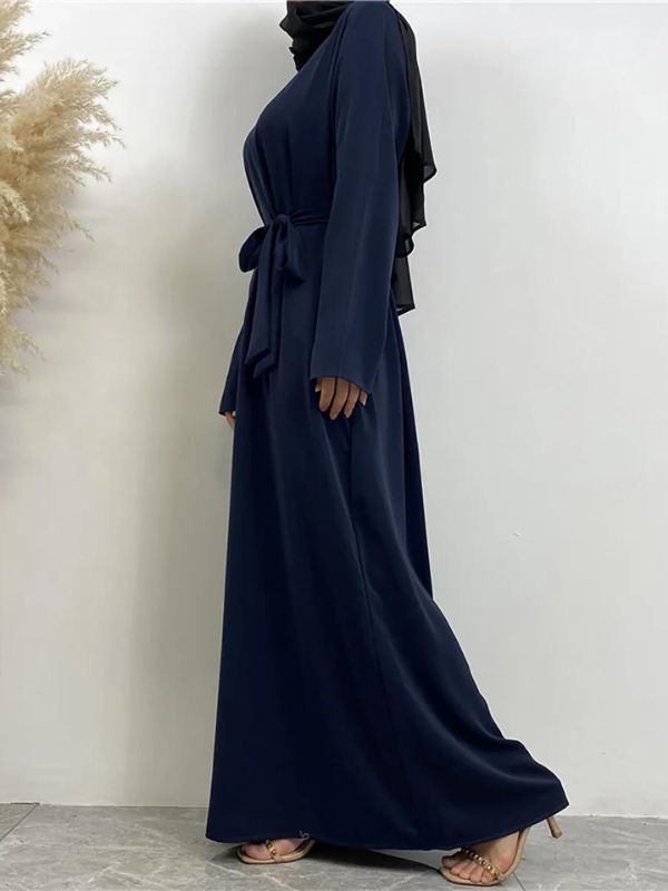 Une femme porte une abaya bleu marine avec une ceinture assortie nouée à la taille, vue de profil. Elle complète sa tenue avec un hijab noir. 