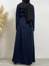 Une femme vue de dos porte une abaya bleu marine avec une ceinture assortie. Elle a un hijab noir drapé élégamment sur ses épaules