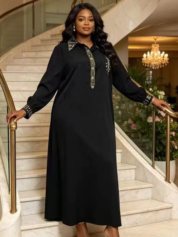 Abaya col chemise noire Nuit de Damas portée de face dans un escalier, col, patte et poignets ornés de strass dorés