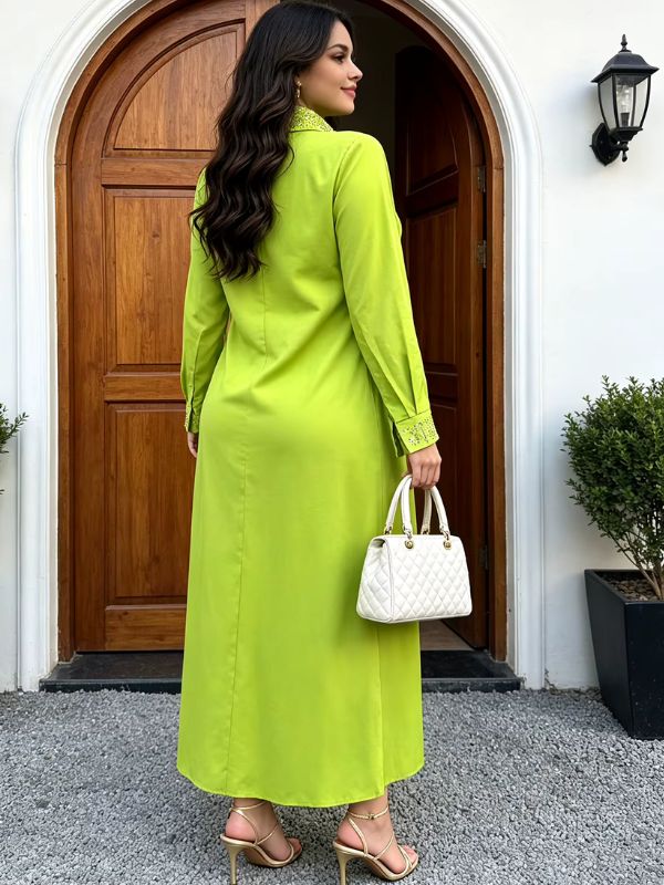 Abaya col chemise vert anis Jardin de Médine vue de dos devant une porte en bois, poignets ornés de strass