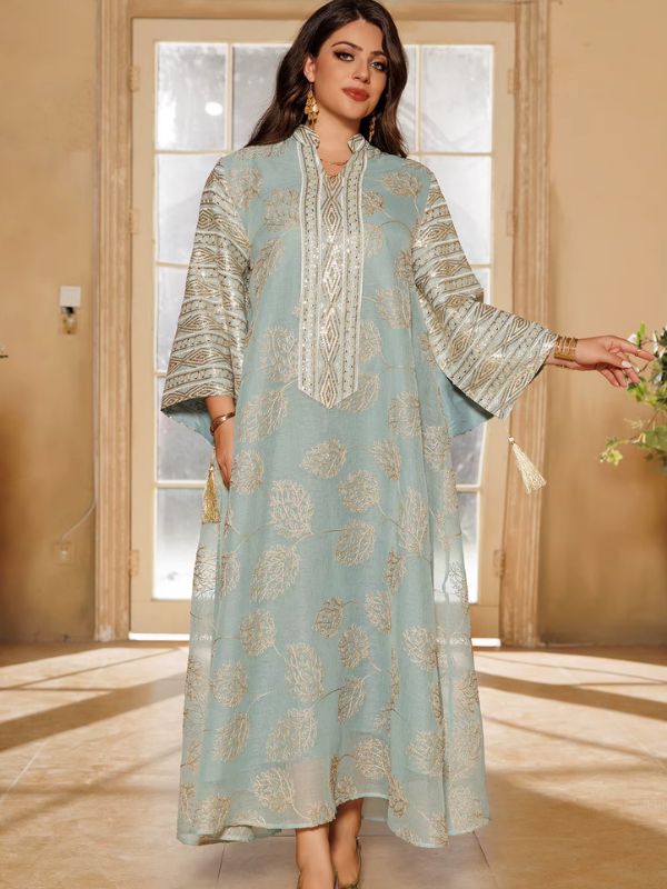 Une femme souriante porte une abaya bleu clair ornée de broderies dorées