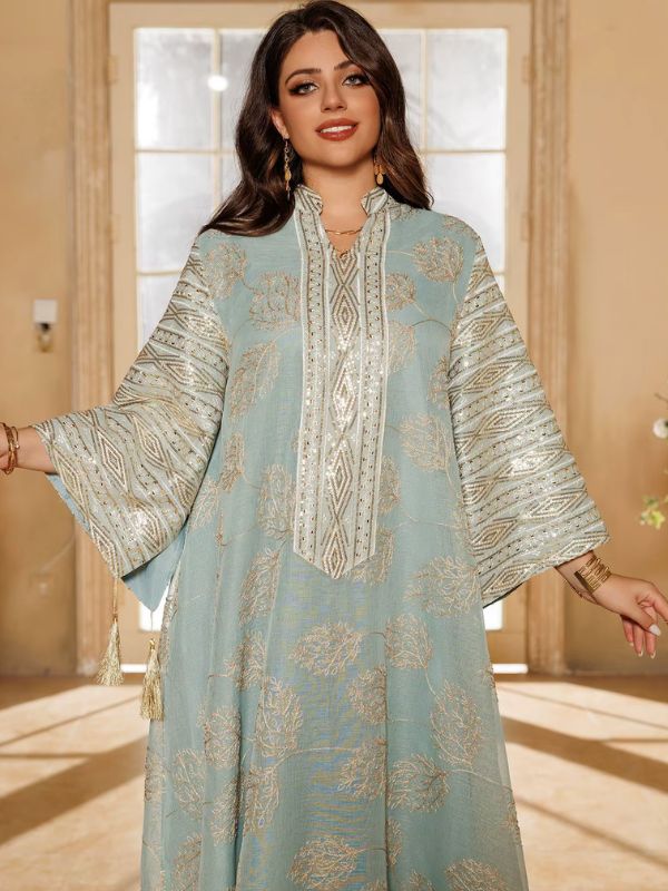Une femme souriante porte une abaya bleu clair ornée de broderies dorées