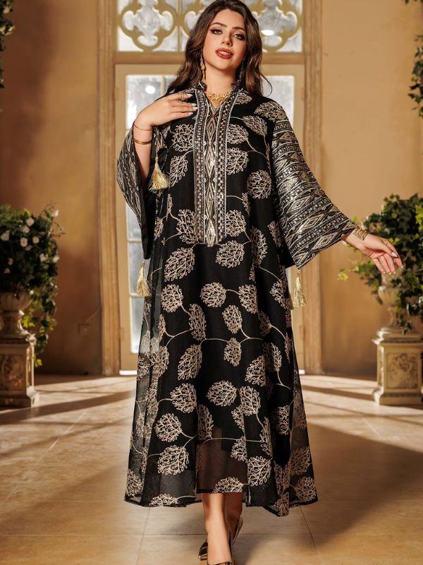 Une femme pose en abaya longue noire décorée de feuillages dorés