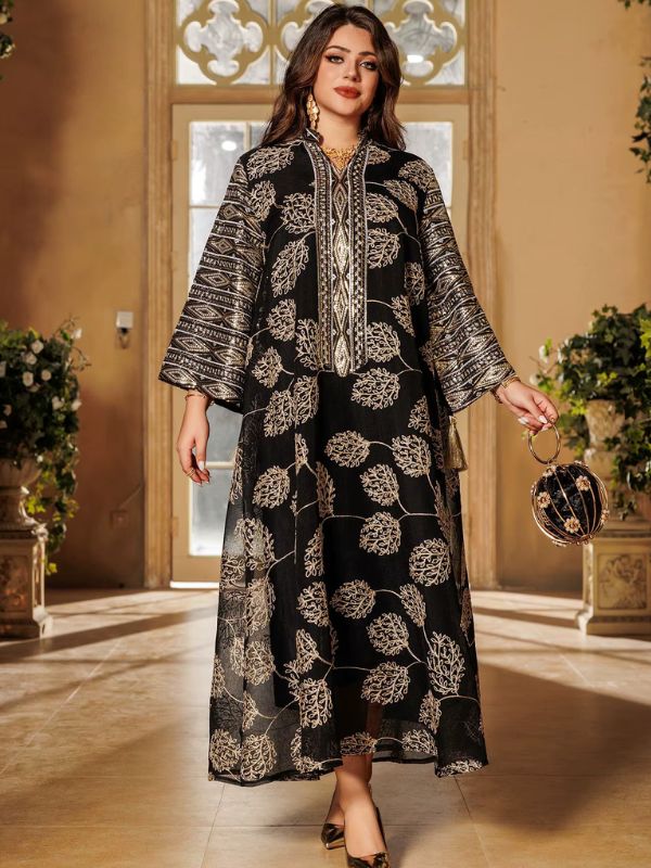 Une femme pose en abaya longue noire décorée de feuillages dorés