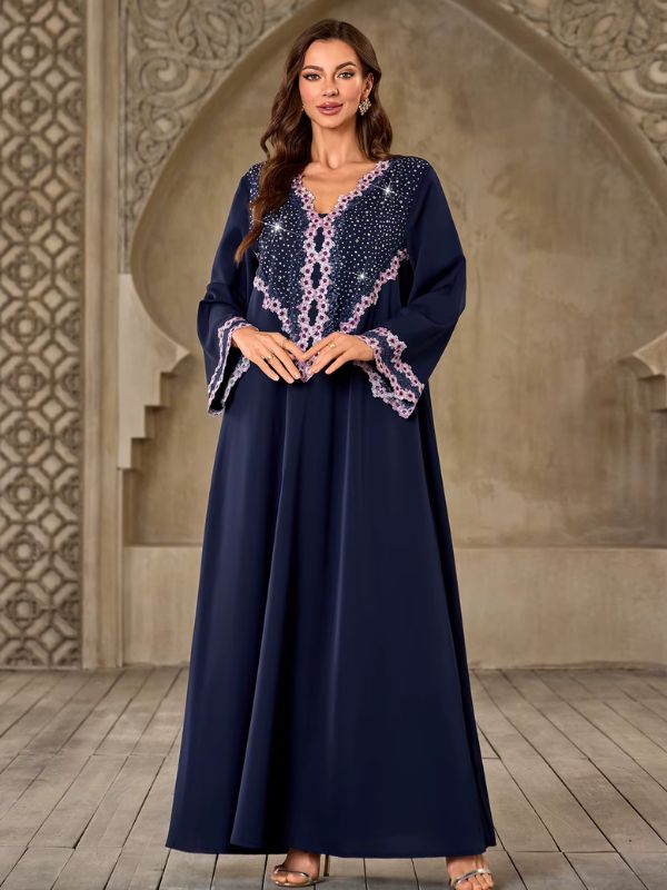 Abaya Dubaï bleu marine, vue de face en pied, mains jointes, col en V orné de dentelle florale rose, strass sur l'empiècement et manches évasées