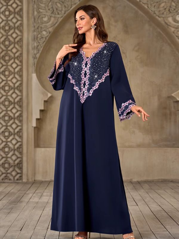 Abaya Dubaï bleu marine, vue de trois quarts, une main posée sur la poitrine, empiècement à strass bordé de fleurs en dentelle rose