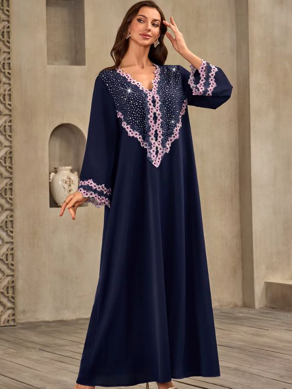 Abaya Dubaï bleu marine, vue de trois quarts devant une niche, une main près de la tête, manche évasée bordée de dentelle florale