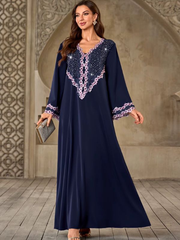 Abaya Dubaï bleu marine, vue de face, mannequin tenant une pochette argentée à paillettes, robe évasée et dentelle florale aux poignets