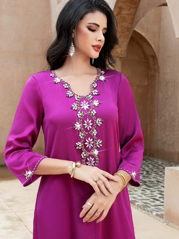 Abaya Dubaï fuchsia, gros plan de face, mains jointes, bande centrale de fleurs de cristal sur la poitrine et manches évasées bordées de strass