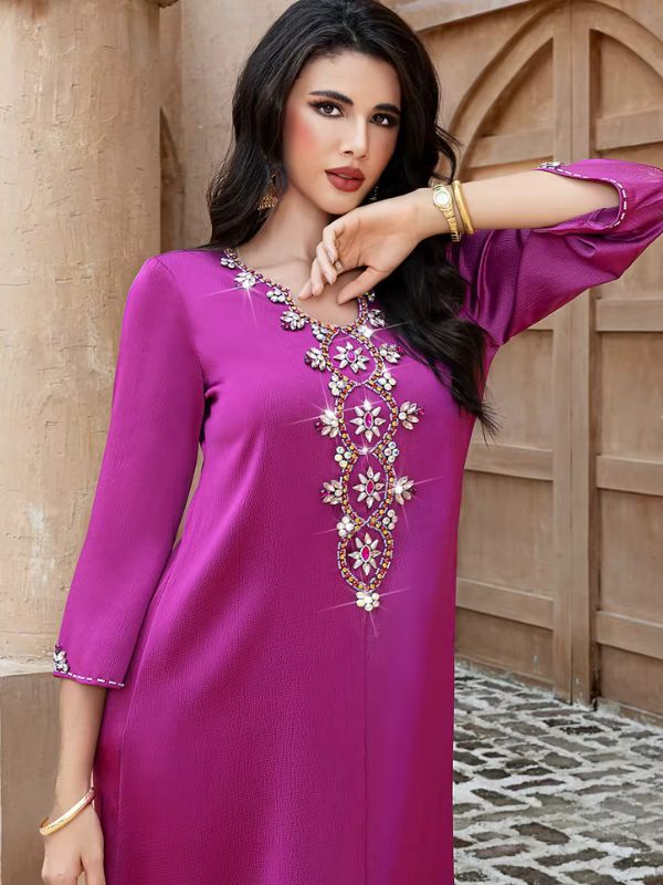 Abaya Dubaï fuchsia, gros plan sur le col en V, main posée sous le menton, chaîne de fleurs de strass aux cœurs roses sur la poitrine