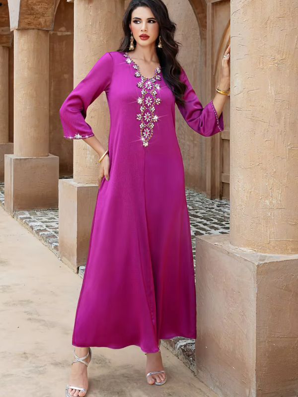 Abaya Dubaï fuchsia, vue de face en pied entre des colonnes, une main posée sur la hanche, robe évasée et bande de fleurs de strass