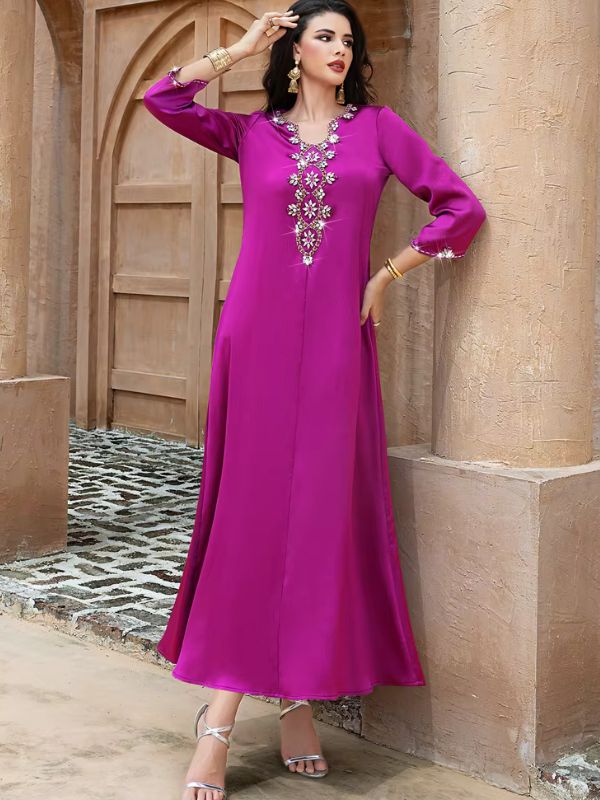 Abaya Dubaï fuchsia, vue de face en pied, adossée à un pilier devant une porte en bois, couture verticale visible au centre du devant