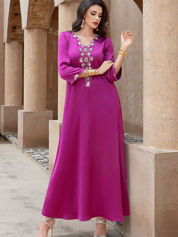 Abaya Dubaï fuchsia, vue de face en pied sous des arcades, un bras replié devant le buste, poignets ornés de strass