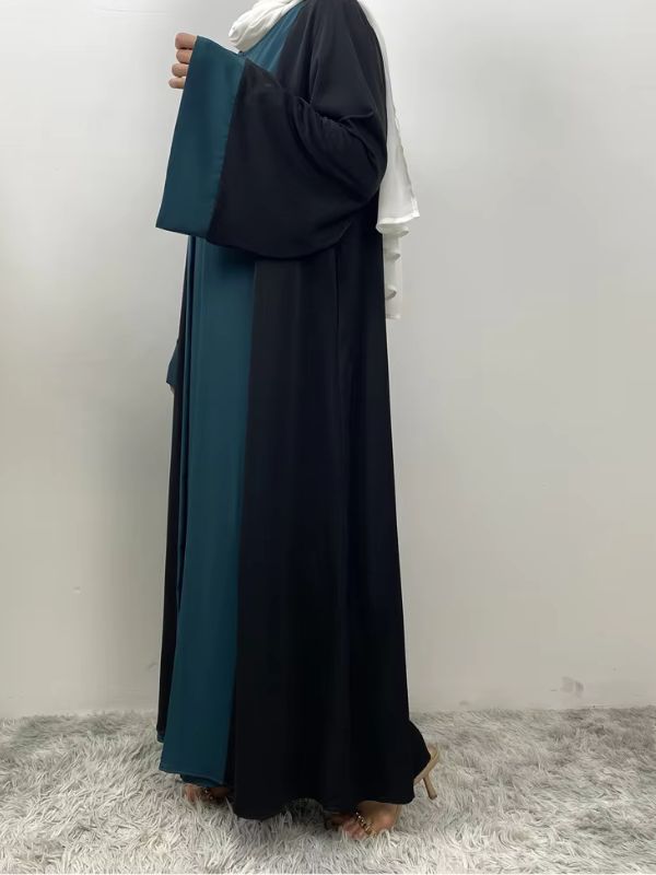 Une femme porte une abaya dubai bleu émeraude et se tient de profil