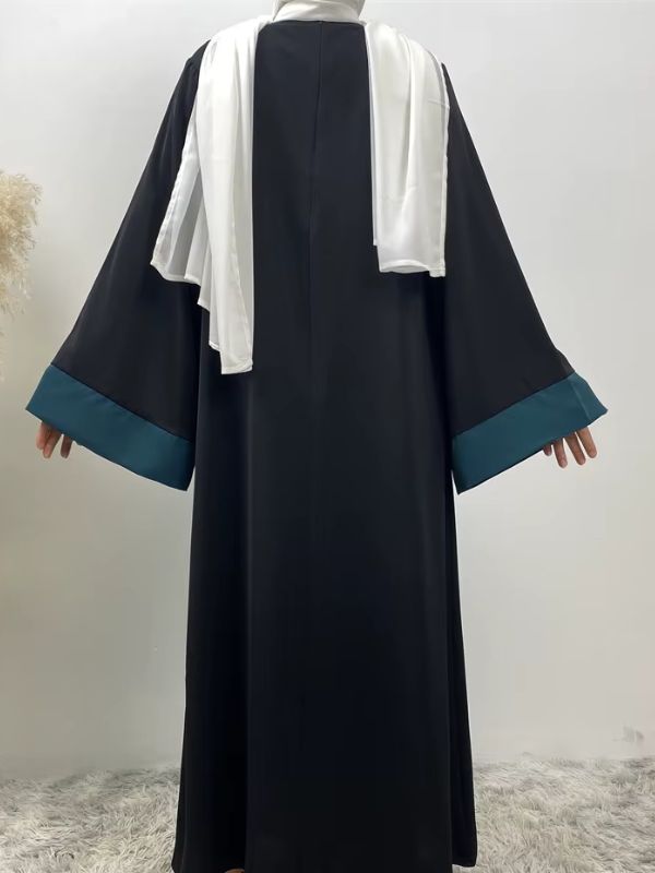 Une femme porte une abaya dubai bleu émeraude et se tient de dos