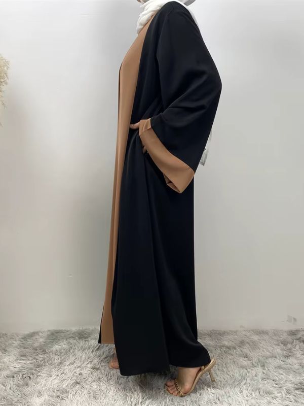 Une femme se tient de profil et porte une abaya couleur caramel et noir