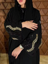 Femme habillée d’une abaya noire décorée de broderies dorées, montrant ses manches en détail