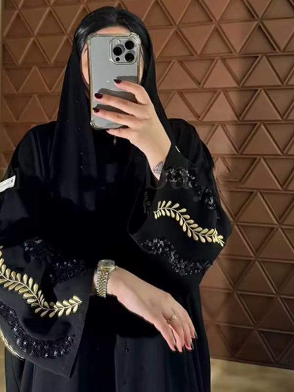 Femme voilée prenant un selfie avec une abaya noire ornée de motifs dorés et sequins sur les manches