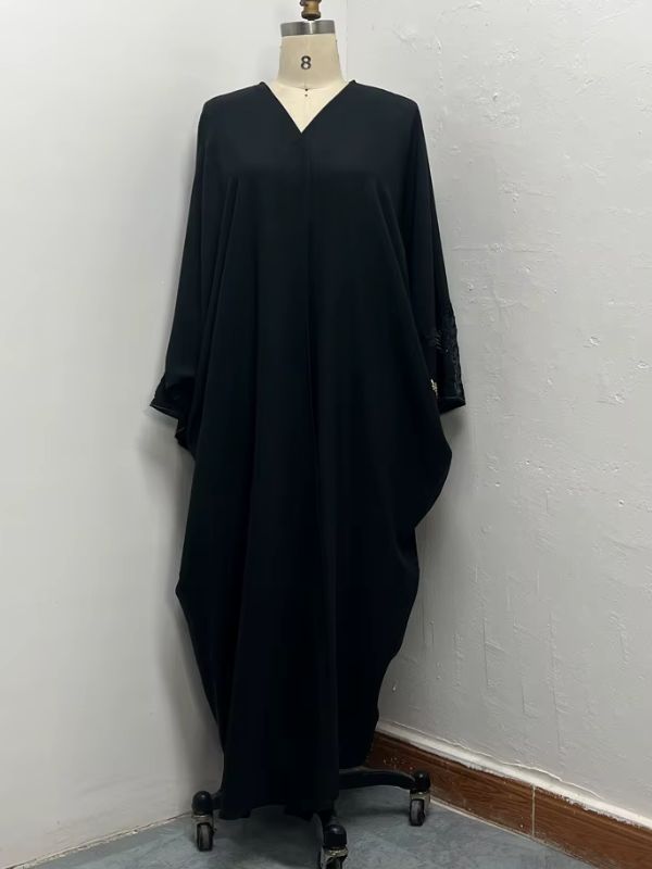 Mannequin présentant une abaya noire simple et fluide sur pied, posée contre un mur clair