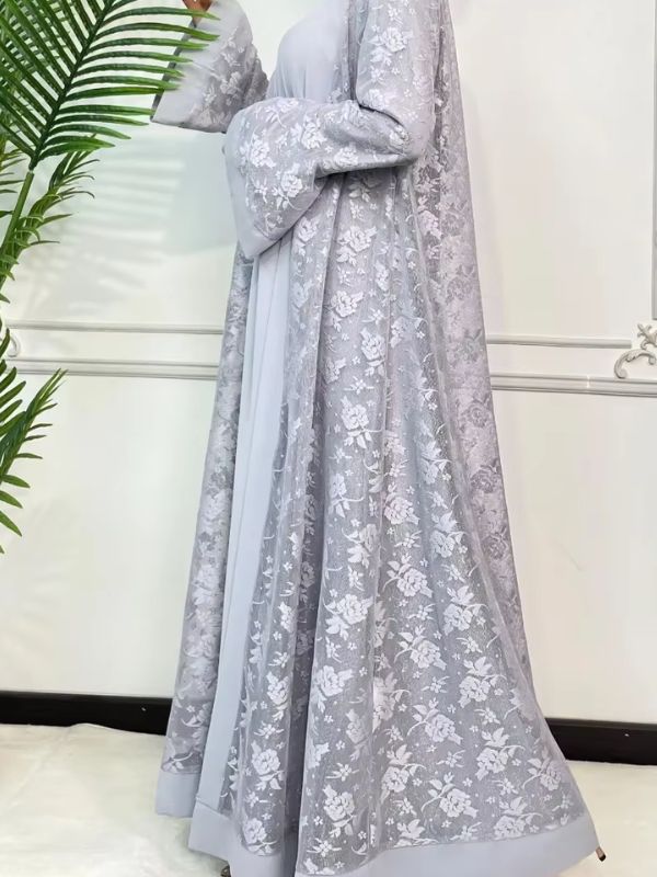 Une femme se tient de profil porte une abaya dubai luxe en dentelle gris perle