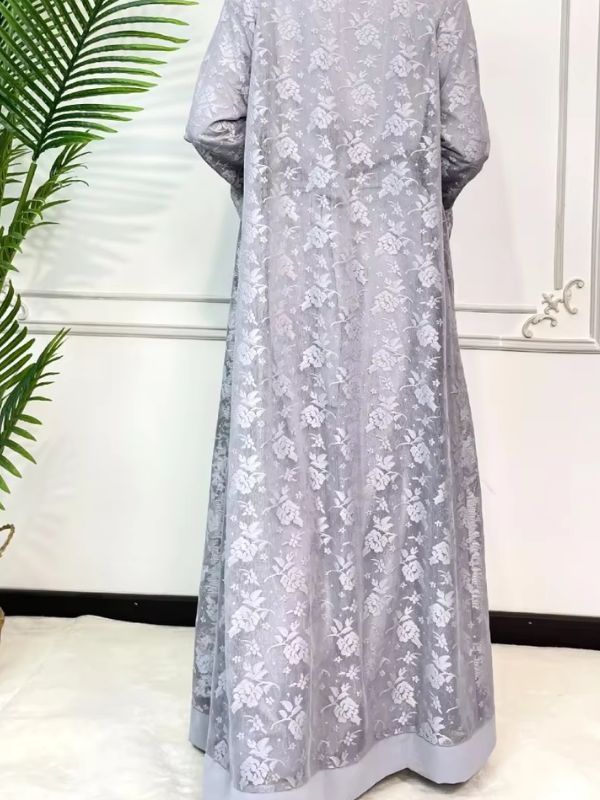 Une femme se tient de dos et porte une abaya dubai luxe gris perle en dentelle