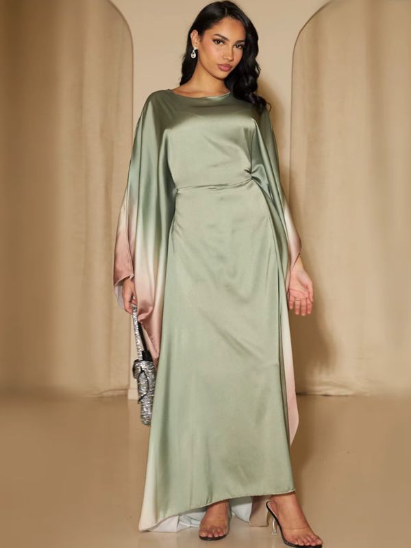 Une femme présente une abaya verte en satin aux manches fluides dégradées rose poudré, posant debout
