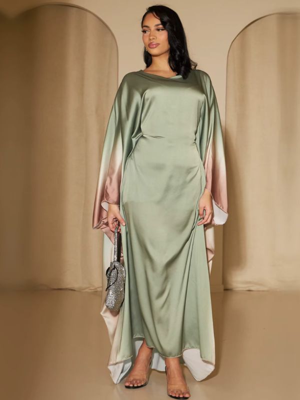 Une femme présente une abaya verte en satin aux manches fluides dégradées rose poudré, posant debout