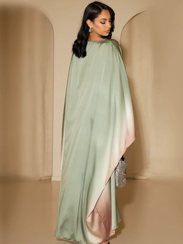 Une femme porte une abaya longue en satin vert sauge avec dégradé rose poudré, vue de dos avec un sac argenté