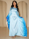 Une femme habillée d’une abaya satinée bleu clair aux manches dégradées bleu profond, tenant un sac perlé
