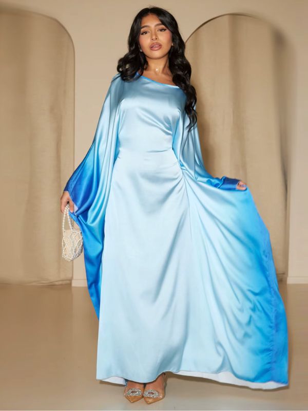 Une femme présente une abaya en satin bleu ciel aux manches fluides dégradées bleu roi, posant élégamment debout