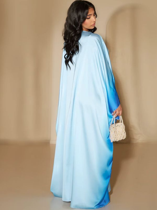 Une femme porte une abaya longue en satin bleu ciel dégradé bleu roi, vue de dos avec un sac perlé blanc