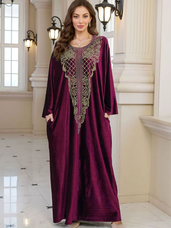 Abaya Dubaï en velours bordeaux, vue de face en pied, plastron brodé de fils dorés, mains dans les poches latérales et manches longues amples