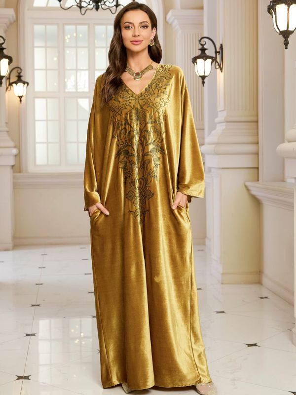 Abaya Dubaï en velours moutarde, vue de face en pied, col en V, broderie florale sur la poitrine, mains dans les poches latérales et manches longues amples