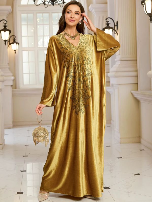 Abaya Dubaï en velours moutarde, mannequin tenant un sac à main doré, col en V et broderie florale sur la poitrine
