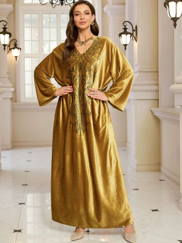 Abaya Dubaï en velours moutarde, vue de face, mains sur les hanches, manches longues amples et broderie florale sur la poitrine
