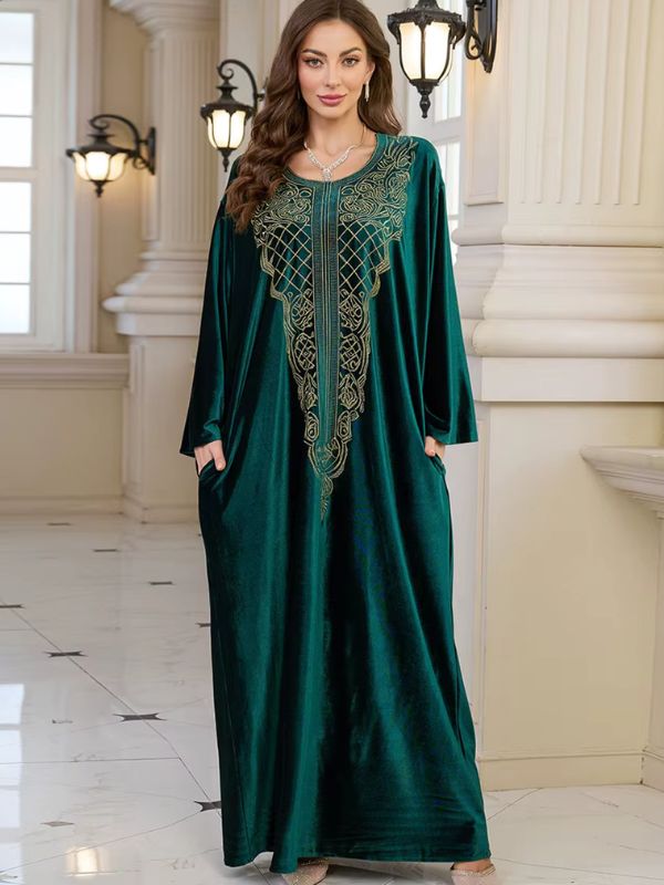 Abaya Dubaï en velours vert bouteille, vue de face en pied, plastron brodé de fils dorés, mains dans les poches latérales et manches longues amples