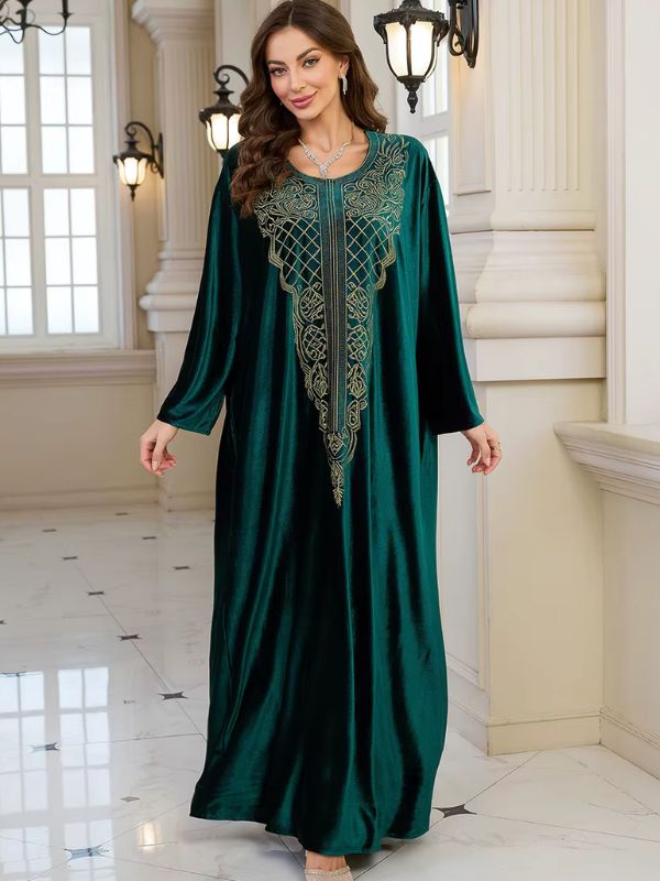 Abaya Dubaï en velours vert bouteille, vue de face, une main dans la poche, plastron brodé de fils dorés et manches longues