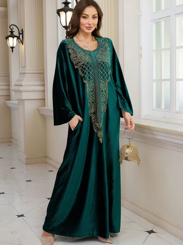 Abaya Dubaï en velours vert bouteille, mannequin tenant un sac à main doré, robe ample et plastron brodé de fils dorés