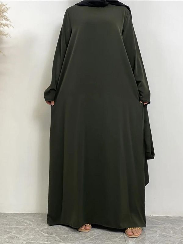 Une femme porte une abaya kaki, combinée avec un hijab noir. La tenue est fluide, couvrant entièrement le corps de manière élégante et modeste. Elle se tient droite, les bras légèrement écartés, mettant en valeur la longueur et la simplicité de la robe. Le fond neutre accentue l'élégance sobre de l'ensemble