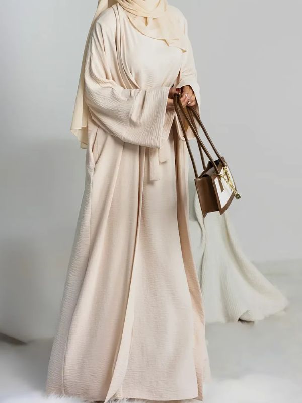 Une femme porte une abaya 2 pièces beige avec un petit sac