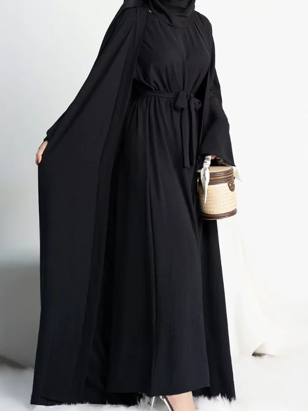 Une femme porte une abaya noire 2 pièces avec un petit sac