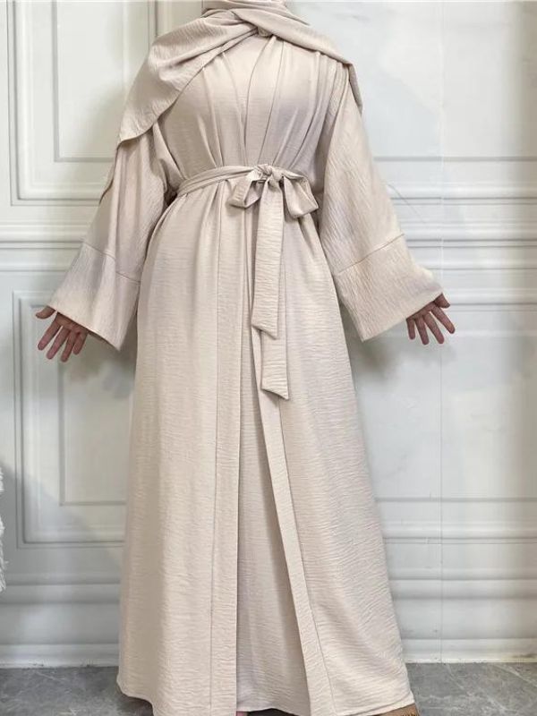 Femme qui porte une abaya kimono dubai beige avec un mur blanc derrière elle et elle porte aussi un hijab