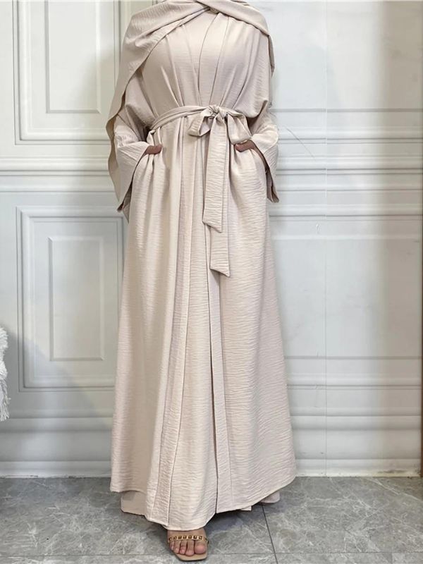 Femme qui porte une abaya kimono dubai beige avec un mur blanc derrière elle et elle porte aussi un hijab