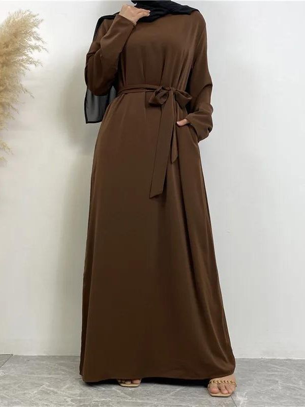 Une femme pose en portant une abaya marron foncé ample et longue