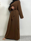 Une femme est vue un peu de profil, portant une abaya marron foncé ceinturée à la taille