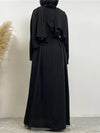 L&#39;image montre une femme portant une abaya noire vue de dos. La robe longue et fluide atteint le sol et est accompagnée d&#39;une ceinture noire nouée à la taille, créant une silhouette élégante et ajustée. La femme porte également un hijab noir, qui tombe gracieusement sur son dos. La simplicité de la tenue est rehaussée par la qualité du tissu et la coupe soignée, offrant une apparence à la fois modeste et sophistiquée