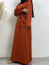 La femme porte une abaya longue de couleur orange vif, vue de profil